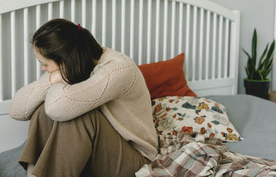 Side view of woman sitting on bed at home