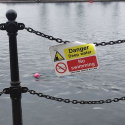 Warning sign on metal chain by river