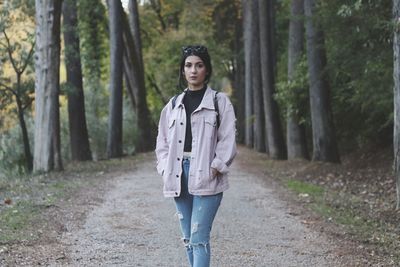 Portrait of young woman standing on road at forest