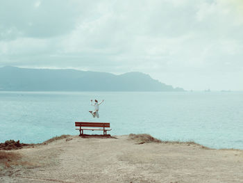 Woman jumping in sea against cloudy sky