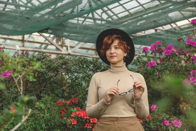 Portrait of beautiful young woman standing by flowering plants