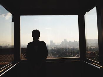 Rear view of silhouette man looking through window