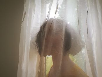 Woman hiding behind curtain at home