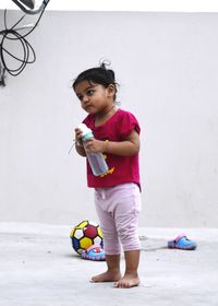 Cute girl holding ball while standing against wall