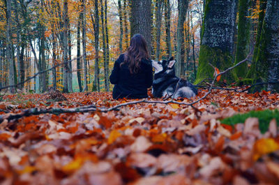 Woman with dog sitting on field in forest