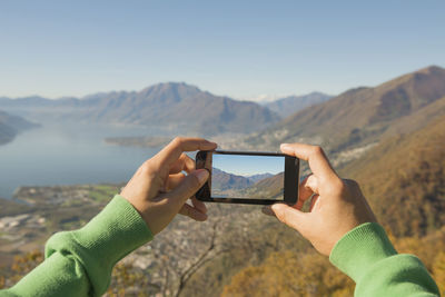 Person photographing with mobile phone against mountain range