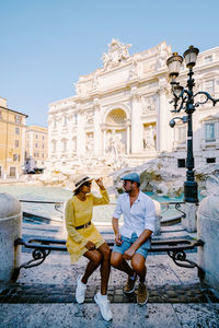 People sitting on historical building against sky in city