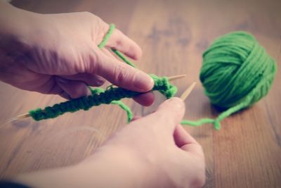 Cropped hands knitting green wool on table at home