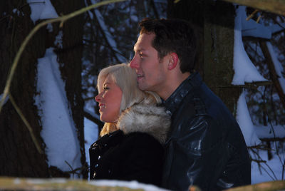 Side view of happy young couple embracing by trees during winter
