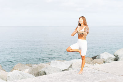 Young woman with long hair in sport clothes practice yoga on sea beach, mental and phisical health