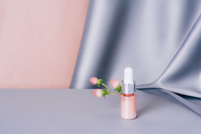 Glass bottle with hypericum on a shiny pink and gray fabric background. serum or essential aroma oil