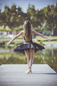 Rear view of woman ballet dancing on pier over lake