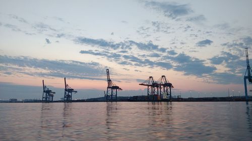 Cranes at commercial dock against sky during sunset