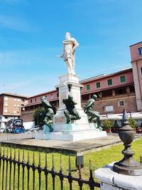 Statue by fountain against building against sky