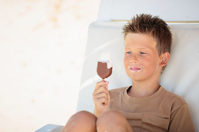 Handsome boy sitting on the beach and eating ice cream