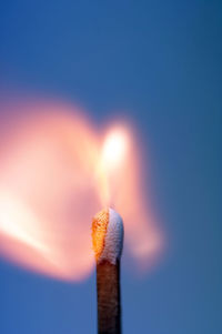 Close-up of burning matchstick over blue background