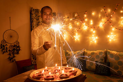 Young man in traditional dress holding the fireworks in hand with ferry lights background