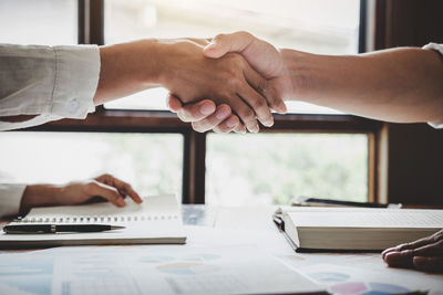 Close-up of businessmen shaking hands over table at office
