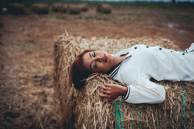 High angle view of young woman lying on hay bale at farm