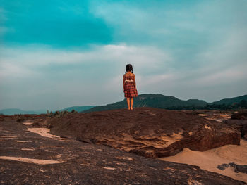 Rear view of girl standing on mountain against sky