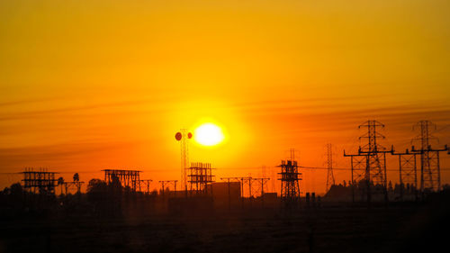 Silhouette electricity pylons against orange sky during sunset
