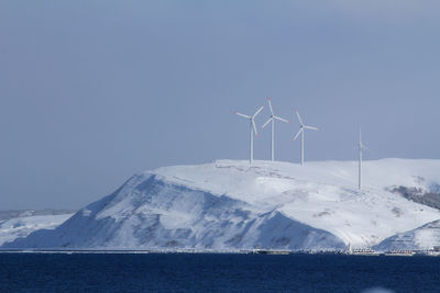 Scenic view of snowcapped mountains with wind turbines against sky