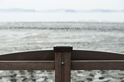 Wooden railing on beach against sky