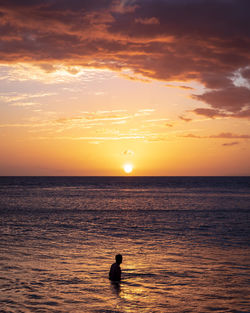 Silhouette people on sea against sky during sunset