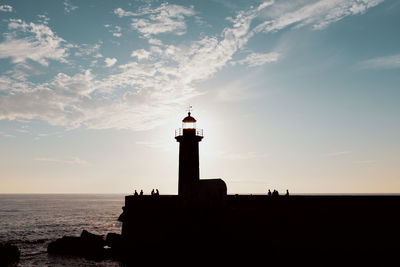 Silhouette lighthouse by sea against sky during sunset