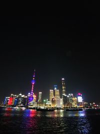 Illuminated buildings by river against sky at night