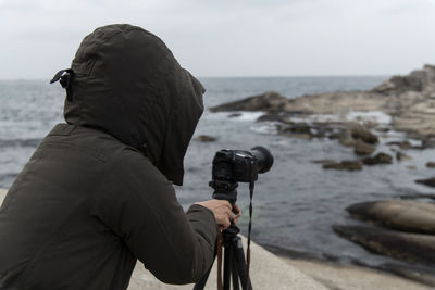 Side view of mature woman photographing sea while standing at beach against sky