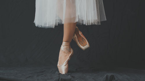 Low section of female ballet dancer dancing against black backdrop