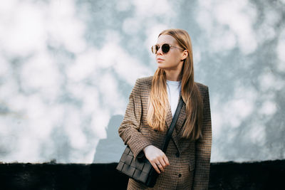 Young woman looking away while standing by wall