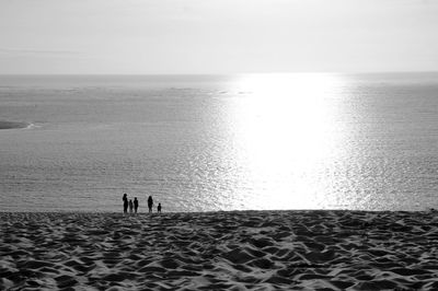 Silhouette people standing at beach against sky during sunny day