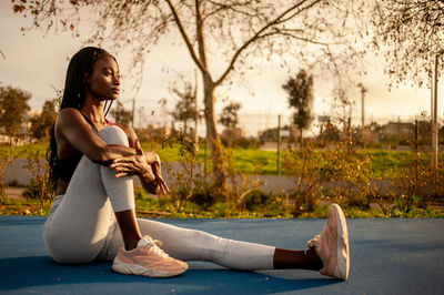 Side view of young woman sitting on plant against trees