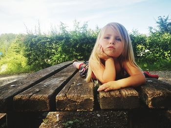 Portrait of girl sitting on wood against trees