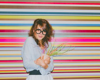Portrait of beautiful woman holding artificial potted plant against multi colored wall