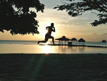 Silhouette man by sea against sky during sunset