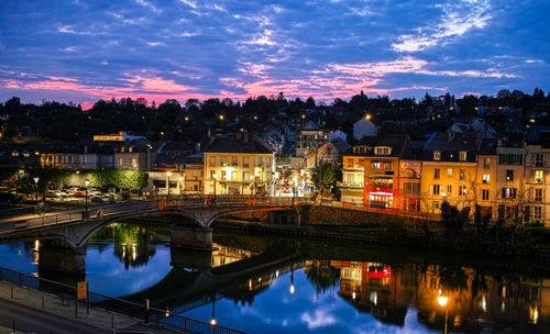 Illuminated buildings by river against sky at night