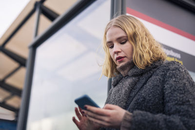 Young woman using phone at tram stop