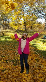 Full length of woman with arms raised standing in autumn
