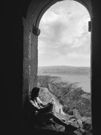 Rear view of woman sitting on window looking at view