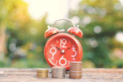 Orange alarm clock and stacked coins on table outdoors