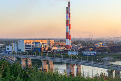 Bridge over river by buildings against sky during sunset