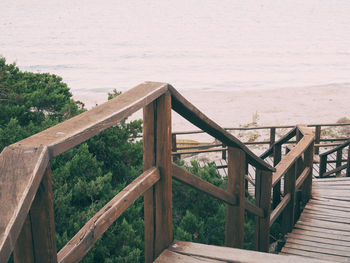 Wooden railing by sea against sky