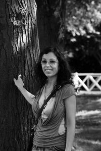 Portrait of smiling young woman standing against tree trunk