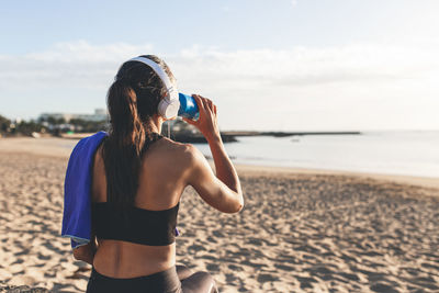 Beautiful fitness woman drinking water after training in front of the beach .