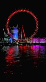 Illuminated ferris wheel by river at night