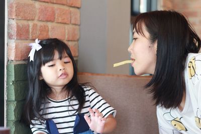 Mother feeding french fries to daughter through mouth