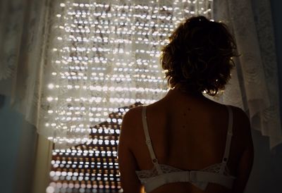 Rear view of woman looking through window at home